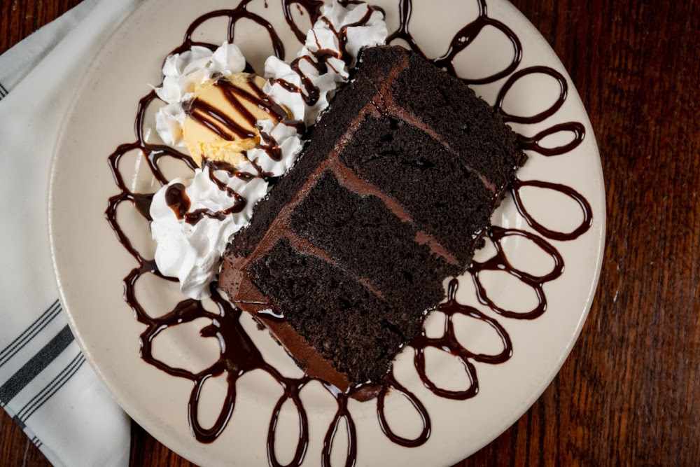 Chocolate cake, served on the chocolate drizzled plate with ice cream and whipped cream